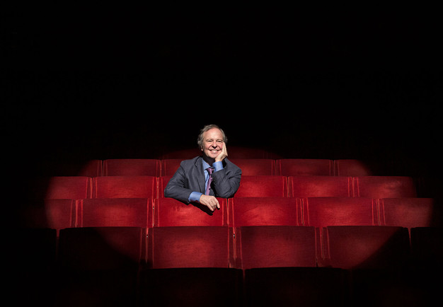 Man som sitter i mitten bland röda stolar. Fotografi