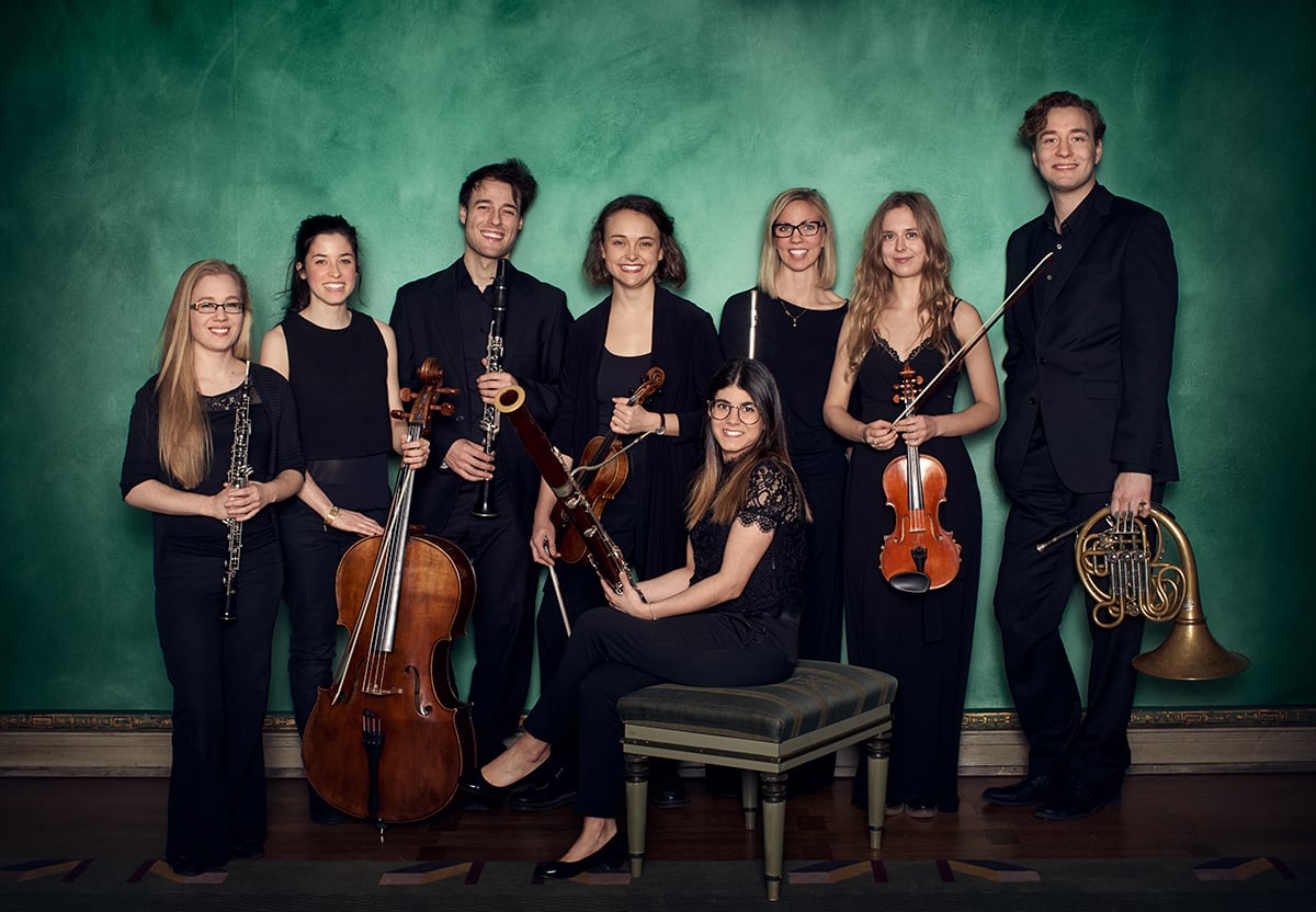 Bild p&aring; en grupp svartkl&auml;dda musiker, de skrattar och h&aring;ller i sina olika instrument, gr&ouml;n bakgrund. . Fotografi.