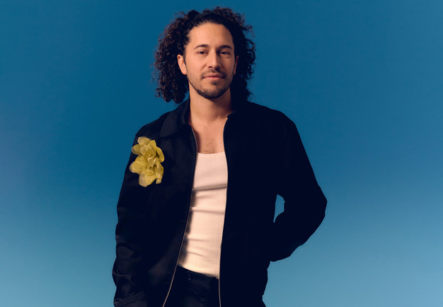 Närbild på man som står framför en blå bakgrund. Fotografi.