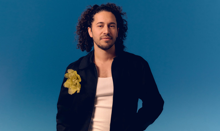 Närbild på man som står framför en blå bakgrund. Fotografi.