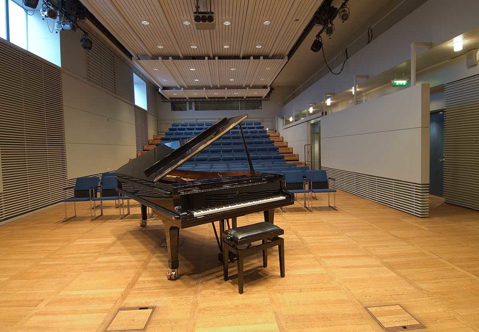 Aulinsalen fotograferad med en flygel i förgrunden. I bakgrunden syns den blåa läktaren.