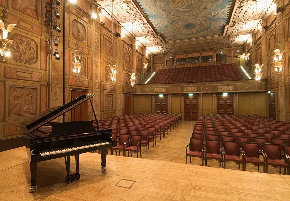 Stor sal med vackra målmningra samt många stolar. Fotografi.