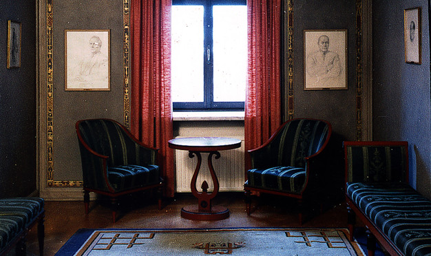 Litet rum med två fåtöljer, två soffor och matta. Fotografi.