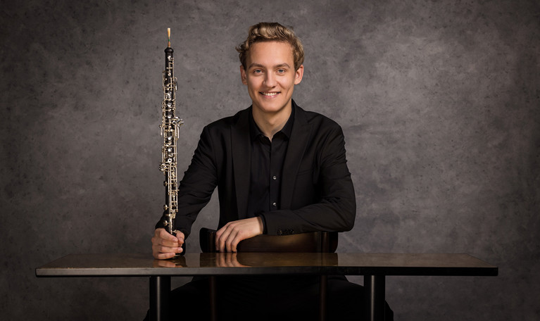 Porträttbild på en leende kvinna med flöjt framför sig. Fotografi.