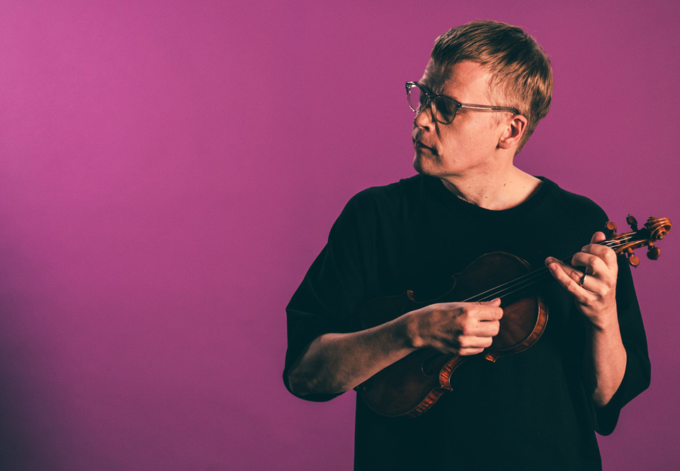 Man som håller i en fiol mot en rosa bakgrund. Fotografi.