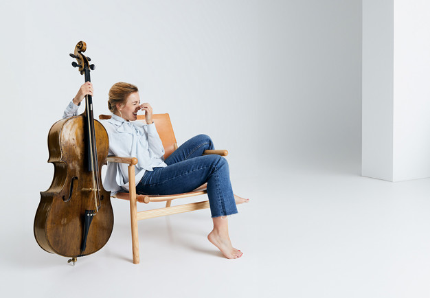Kvinna som sitter på en stol med en cello. Fotografi