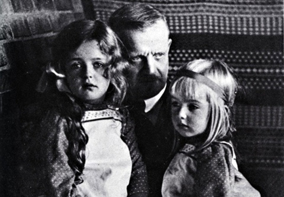 Man med två små barn i sitt knä. Fotografi.